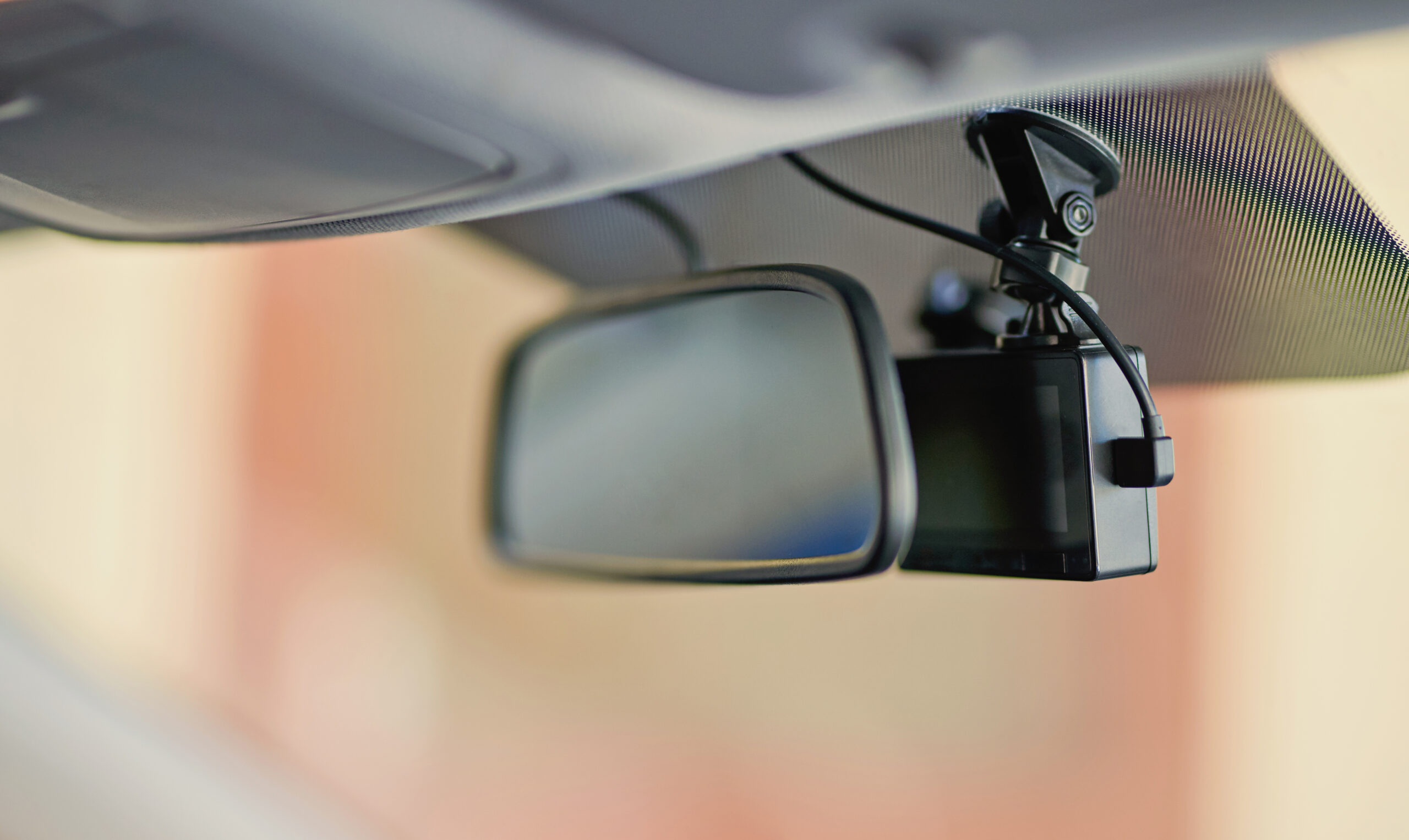 Image showing a dash cam mounted behind rear view mirror with power cable going up into car's headliner