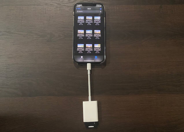 micro SD card inside a microSD to SD adapter, which is plugged into an Apple Lightning to SD Card Camera reader, which is plugged into an iphone with dash cam videos displayed on the screen.