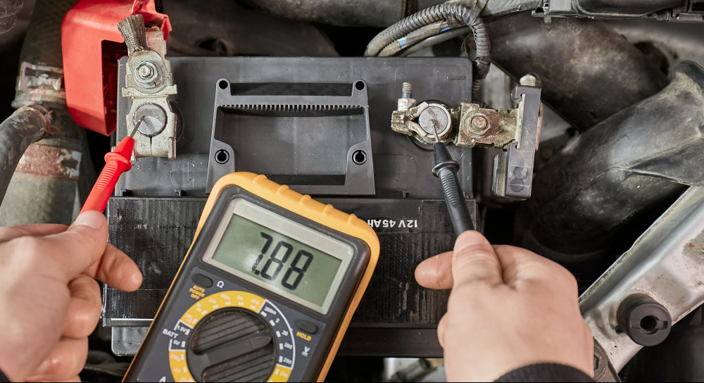 Person testing car voltage with multimeter. Multimeter probes are on the battery terminal and the multimeter reads 7.88 volts.