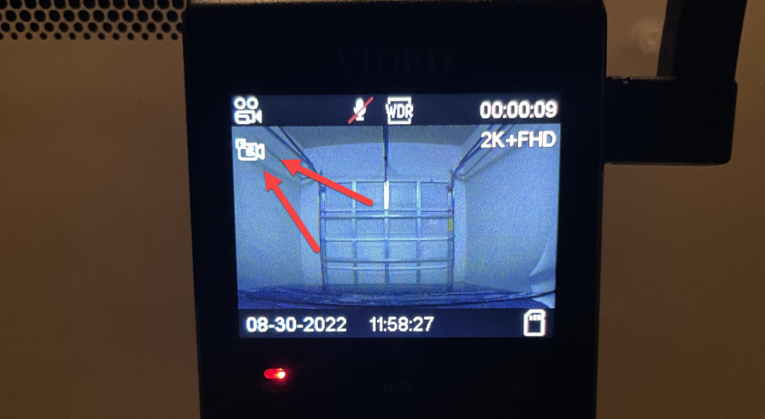 A picture of the screen of a dash cam with two red arrows pointed towards the Parking Mode icon. There is a closed garage door on the dash cam screen.